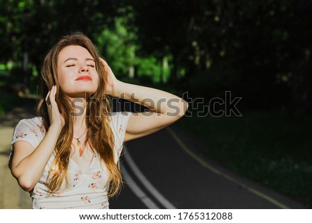 Portrait young woman in white top touching her hair and enjoying sun light  on the drive way in the park . Solo outdoor activity. End quarantine. Alone teenage girl in the nature. Close up 