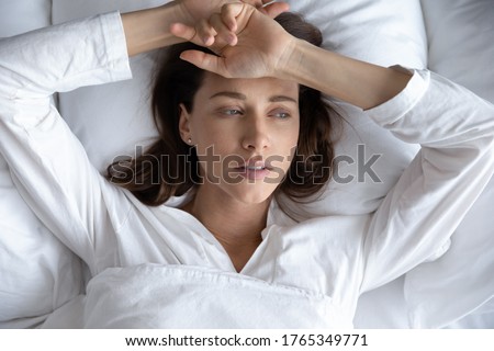 Top view of depressed sad young woman lie relax in bed look in distance thinking remembering, upset stressed millennial female rest in home bedroom feel sick suffer from illness or depression Royalty-Free Stock Photo #1765349771