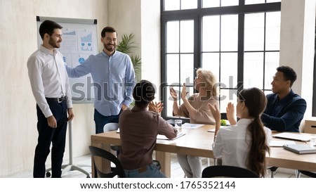 Smiling executive introducing new hired employee at corporate meeting, congratulating successful businessman with job promotion, thanking for good work result, diverse colleagues applauding Royalty-Free Stock Photo #1765352144