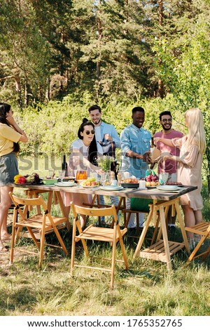 Large group of happy young intercultural friends unpacking bags with food products from supermarket while serving table for outdoor dinner Royalty-Free Stock Photo #1765352765