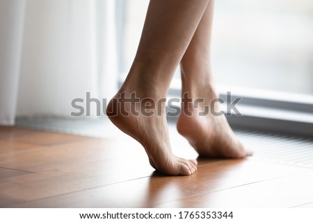 Crop close up of young woman barefoot step on warm wooden floor in bedroom or living room, female feet legs walk in room with underfloor electric heating at modern home or house Royalty-Free Stock Photo #1765353344