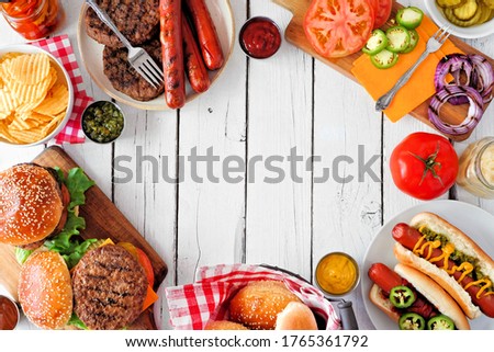 Summer BBQ food frame with hot dog and hamburger buffet. Overhead view against a white wood background. Copy space.