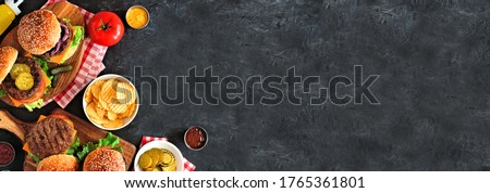 BBQ hamburger corner border. Top down view table scene over a dark slate banner background. Copy space. Royalty-Free Stock Photo #1765361801