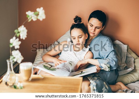 Mother and daughter enjoy in bed at home. Morning awakening. mother and daughter reading a book together in bed in the morning 