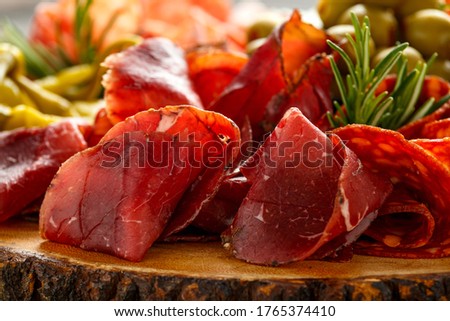 Dry cured fermented beef and pork meat cocktail selection with salami, chorizo, cheese, olives and grapes served on wooden board Royalty-Free Stock Photo #1765374410