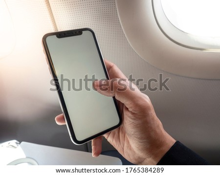 Holding mobile smart phone on aircraft seat next to window. Aircraft tray table with sunlight from window.