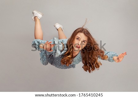 Beautiful girl levitating in mid-air, falling down and her hair messed up soaring from wind, model flying hovering with dreamy peaceful expression. indoor studio shot isolated on gray background Royalty-Free Stock Photo #1765410245