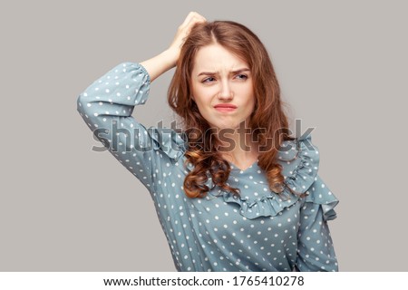 Hmm, need to think! Thoughtful confused brunette girl ruffle blouse scratching head having doubts, not sure contemplating with uncertain puzzled face. indoor studio shot isolated on gray background Royalty-Free Stock Photo #1765410278