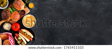 Summer BBQ food side border with hot dog and hamburger buffet. Top down table scene over a dark slate background. Copy space.