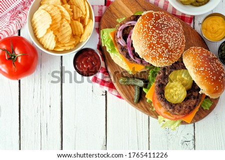 BBQ hamburgers with potato chips. Overhead view table scene on a white wood background. Royalty-Free Stock Photo #1765411226