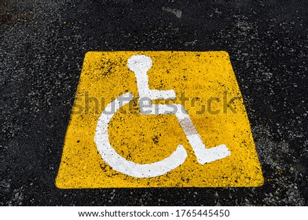 a yellow sign on the asphalt shows a Parking place for people with disabilities, a road sign, markings on the road