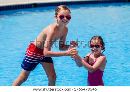 Kids boy and girl holding juice in the swimming pool. Childhood, summer and holiday concept