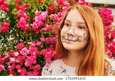 Outdoor close up portrait of happy young girl, wearing eyeglasses, posing in flower garden