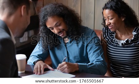 African ethnicity 35s couple sign contract document closing deal with real estate agent sit in public place cafe. Happy spouses put signature on agreement taking obligations with banker getting loan Royalty-Free Stock Photo #1765501667