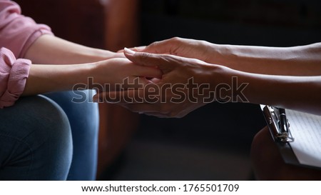 Different ethnicity female friends hold hands during confidential talk close up. Counsellor psychologist provide mental aid to patient at session in clinic, addicted patient professional help concept Royalty-Free Stock Photo #1765501709
