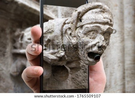 Gargoyle on Marienplatz, Munich, Bavaria, Germany. Picture of detail of Munich landmark on smartphone screen, funny photo of Gothic gargoyle and mobile or cell phone. Concept of travel and technology.