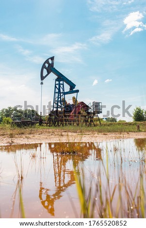 Oil and gas industry. Working oil pump jack on a oil field with reflection on a puddle. White clouds and blue sky. Oil production