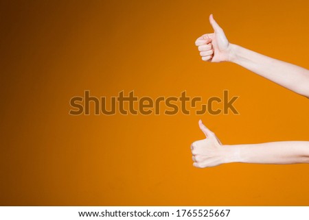 Female hands showing thumbs up in approval on an orange background. Slender female hands showing sign like