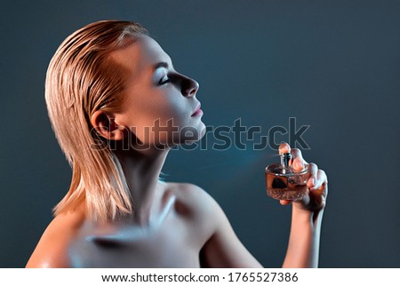 Beautiful girl with blond hair, puts perfume on the body. Gray background. Beauty concept.