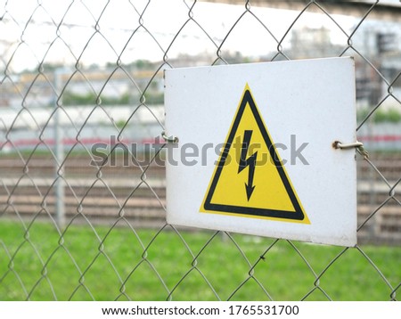 Electricity caution sign on trellised fence, on blurred city background, danger sign
