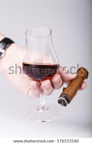 Old brandy or rum in glass and cigar in male hand on white background