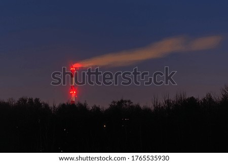 Factory chimney signaled with red lights above a dark forest at night.
