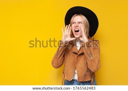 young girl in fashionable autumn clothes screaming on a yellow isolated background, a woman in a jacket and hat says a place for text