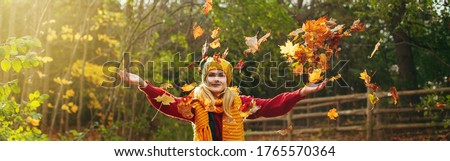 Caucasian happy smiling woman girl in warm yellow scarf and hat throwing autumn fall orange red leaves in park forest outdoor. Seasonal activity lifestyle outside. Web banner header for website. Royalty-Free Stock Photo #1765570364
