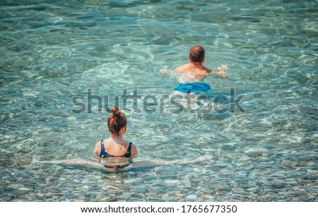 Honey moon on the sea shore. Back view of loving couple bathing together on beautiful beach. Brunette woman doing yoga in the sea watching her husband floating
