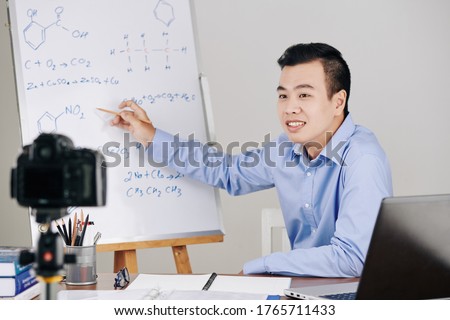 Science teacher drawing chemical formulas on whiteboard when hosting online lesson for college students
