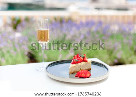 Summer breakfast in restaurant. Still life with wineglass of champagne, strawberry cheesecake. Cafe in lavender garden. Delicious french food and drink. Intimate romantic celebration in quarantine.