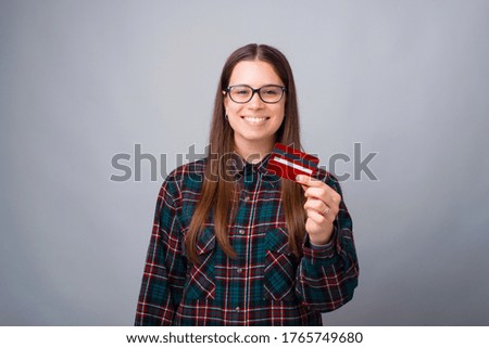 Photo of smiling young woman showing red debit card over white wall.