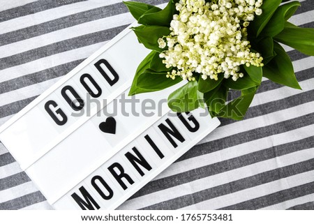 Lightbox with text GOOD MORNING and bouquet lilies of the valley in white bucket, spring time, holiday background