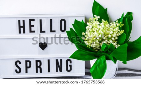Lightbox with text HELLO SPRING and bouquet lilies of the valley in white bucket, spring time, holiday background