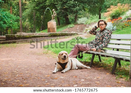 A girl and a Labrador Retriever sit on a bench in an empty Park against the background of a fountain. Morning walk with the dog