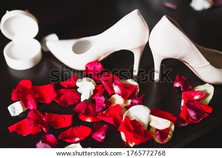 Beautiful toned picture with wedding rings on wedding shoes against the background of flowers