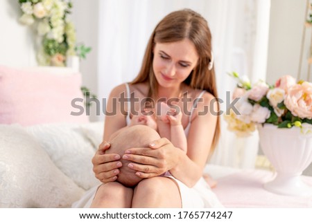 a young beautiful mother holds her daughter a girl of 6 months on her lap on a white bed, playing and kissing her, place for text