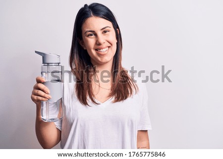 Young beautiful brunette woman drinking bottle of water over isolated white background looking positive and happy standing and smiling with a confident smile showing teeth