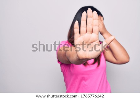 Young beautiful brunette woman wearing casual pink t-shirt standing over white background covering eyes with hands and doing stop gesture with sad and fear expression. Embarrassed and negative concept