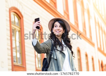 Carefree and happy, sunny spring mood. Cute young smiling girl is making selfie on a camera while walking outdoors. She is wearing casual outfit