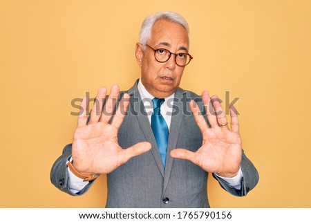 Middle age senior grey-haired handsome business man wearing glasses over yellow background Moving away hands palms showing refusal and denial with afraid and disgusting expression. Stop and forbidden.