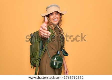 Young blonde explorer woman with blue eyes hiking wearing backpack and water canteen smiling friendly offering handshake as greeting and welcoming. Successful business. Royalty-Free Stock Photo #1765792532