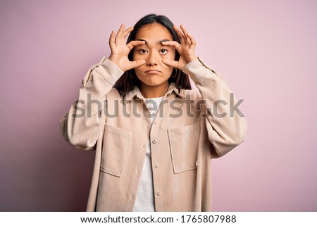 Young beautiful asian woman wearing casual shirt standing over pink background Trying to open eyes with fingers, sleepy and tired for morning fatigue