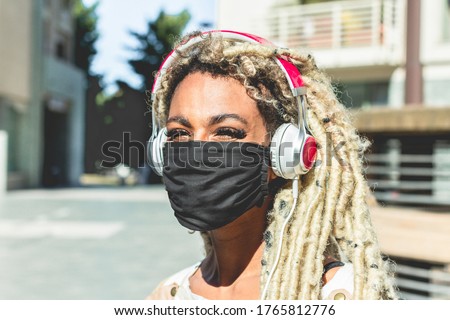Portrait of african girl moving blond dreadlocks hair listening music while wearing face protective mask for Coronavirus prevention - Covid 19 lifestyle and trendy people concept - Main focus on eyes Royalty-Free Stock Photo #1765812776
