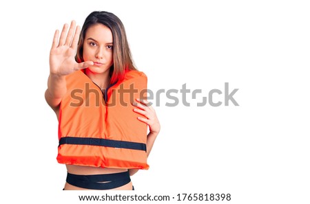 Young beautiful girl wearing life jacket with open hand doing stop sign with serious and confident expression, defense gesture 