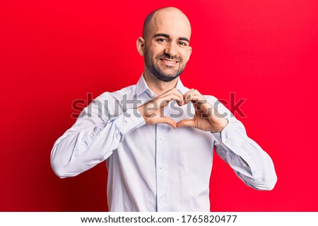 Young handsome bald man wearing elegant shirt smiling in love doing heart symbol shape with hands. romantic concept. 