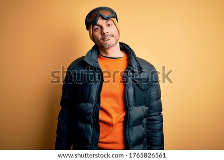 Young handsome skier man skiing wearing snow sportswear using ski goggles looking sleepy and tired, exhausted for fatigue and hangover, lazy eyes in the morning.