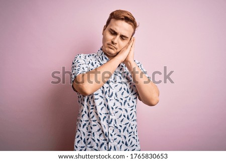 Young handsome redhead man wearing casual summer shirt standing over pink background sleeping tired dreaming and posing with hands together while smiling with closed eyes.