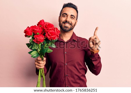 Young hispanic man holding flowers smiling happy pointing with hand and finger to the side 