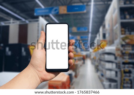 Online shopping using your phone. Mockup Smartphone with a white screen in hand close up on the background of shelving in a supermarket